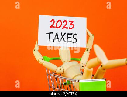 2023 Steuern Neujahr Symbol. White Paper mit Worten 2023 Steuern, menschliches Modell im warenkorb. Schöne orange Tisch orange Hintergrund. Business und 2023 Ta Stockfoto