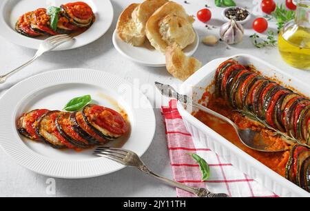 Köstliche Ratatouille in Backform und Teller auf weißem Tisch, Dinner-Konzept Stockfoto