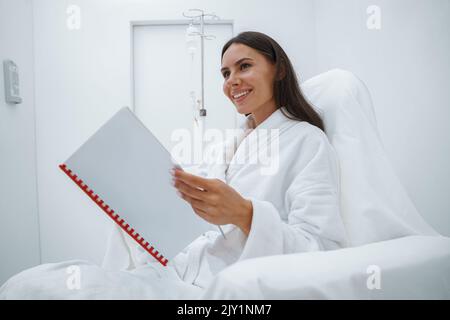 Schöne Frau im weißen Bademantel Lesemagazin, während sie im luxuriösen Wellness Spa-Center sitzt Stockfoto