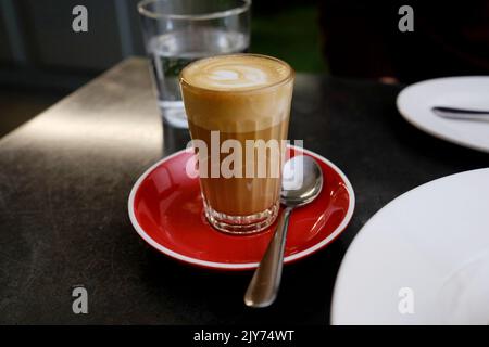 Ein Piccolo-Kaffee in einem Glas auf einer roten Untertasse im Bella Brutta, einem modernen italienischen australischen Restaurant in Newtown, Sydney - New South Wales, Australien Stockfoto