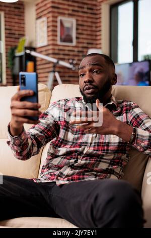 Junger Mann, der an einer Online-Videocall-Konferenz teilnimmt und über eine Smartphone-App mit Menschen in einer Videokonferenz spricht. Freiberuflicher Chat bei Remote-Telefonkonferenzen über ein Mobiltelefon. Stockfoto