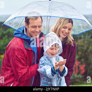Hes fasziniert vom Regen. Eine dreiköpfige Familie steht draußen im Regen. Stockfoto
