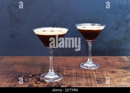 Gläser Espresso martini mit Kaffeebohnen auf Holztisch und schwarzem Hintergrund Stockfoto