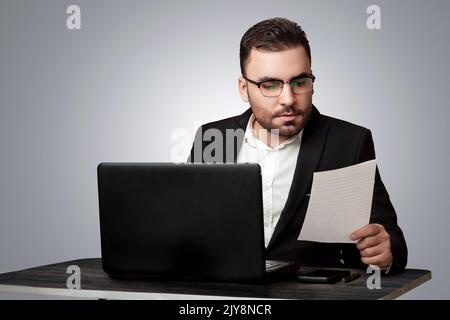Ein hart arbeitender Mitarbeiter, der seine Arbeit an seinem Schreibtisch verrichtete, in einem formellen Anzug und einem abgeschiedenen Hintergrund gekleidet, Geschäftsmann Stockfoto