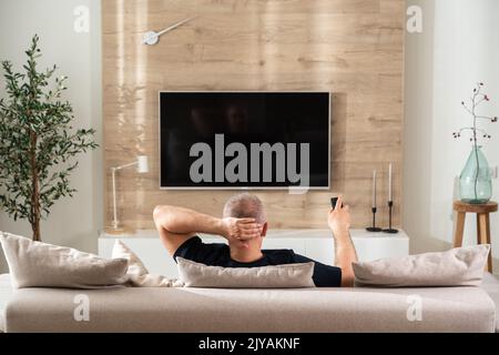 Rückansicht des Mannes vor dem Fernseher im modernen Wohnzimmer Stockfoto