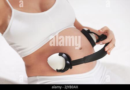 Beruhigende Melodien für einen wachsenden Bauch. Eine Schwangere hält Kopfhörer um ihren Bauch. Stockfoto