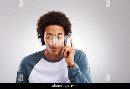 Schließen Sie die Augen, und lassen Sie sich von Musik befreien. Studioaufnahme eines jungen Mannes, der vor grauem Hintergrund Musik auf seinen Kopfhörern hört. Stockfoto