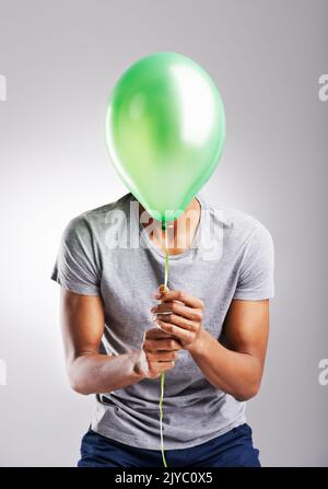 Lass los und lass dich frei. Ein Mann bedeckt sein Gesicht mit einem Ballon auf einem grauen Hintergrund. Stockfoto