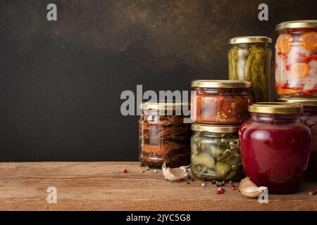 Gemüse für den Winter konservieren, Gemüse in Dosen auf einem Holztisch gegen eine braune Wand, eingelegtes oder fermentiertes Gemüse, Platz kopieren Stockfoto