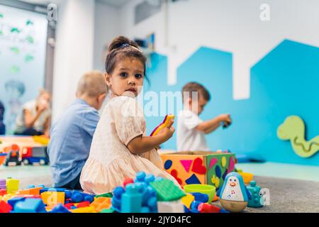 Spielzeit im Kindergarten. Kleinkinder sitzen auf dem Boden und spielen mit Bausteinen, bunten Autos und anderen Spielzeugen. Wie man mit anderen interagiert und lebenswichtige Fähigkeiten entwickelt. Hochwertige Fotos Stockfoto