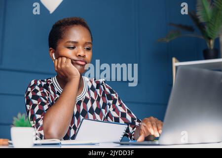 Verärgert schwarz lockig weibliche freiberuflich Blick auf Laptop sitzen am Bürotisch. Leiden unter starken Kopfschmerzen oder Migräne. Müde junge ethnische Frau Stockfoto