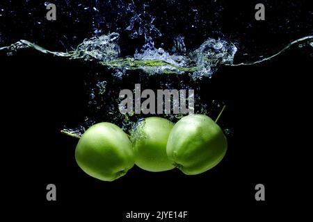 Gruppe von grünen Äpfeln, die in Wasser fallen, mit Spritzern und Blasen auf schwarzem Hintergrund isoliert. Stockfoto