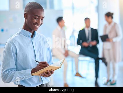 Assistent schreibt Notizen in einem Notizbuch für ein Team von Führungskräften und ist mit einer positiven Einstellung, Vision und Mission zufrieden. Afroamerikanisch Stockfoto