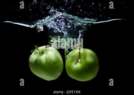 Zwei grüne Äpfel, die auf schwarzem Grund isoliert wurden, fielen ins Wasser Stockfoto