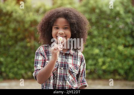 Glückliches afroamerikanisches Mädchen mit einem Lutscher in den Händen im Garten oder im Freien. Stockfoto