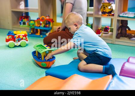 Spielzeit im Kindergarten. Kleinkinder sitzen auf dem Boden und spielen mit bunten Plastikautos, Booten und anderen Spielzeugen. Hochwertige Fotos Stockfoto