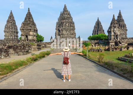 Indonesien, Prambanan – junges Mädchen mit Hut, der mit offenen Armen steht und während des Sonnenuntergangs den Prambanan-Tempel sieht. Asiatische Frau mit weißem Kleid und trägt ha Stockfoto