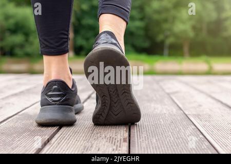 Nahaufnahme von Frauenbeinen in schwarzen Sneakers, die auf einem Holzdeck laufen Stockfoto