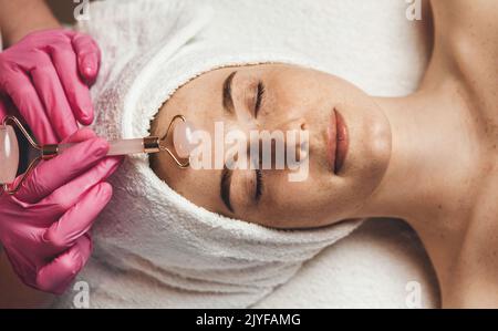 Draufsicht auf eine kaukasische Frau, die im Spa-Salon mit Jade Face Roller massiert wurde. Sommersprossen. Kosmetik, Körper- und Hautpflege. Vakuumwalze Stockfoto