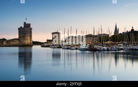 Blick auf den alten Hafen der französischen Stadt La Rochelle bei Sonnenuntergang mit Schiffen vor Anker im Hafen und den beiden Türmen im Hintergrund. Stockfoto