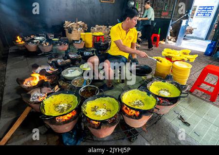 Ein Mann Baker macht Banh Xeo auf den umliegenden Brazierern, vegetarische Pfannkuchen, die Buddhisten dienen und den Tempel in an Giang, Vietnam, besuchen Stockfoto