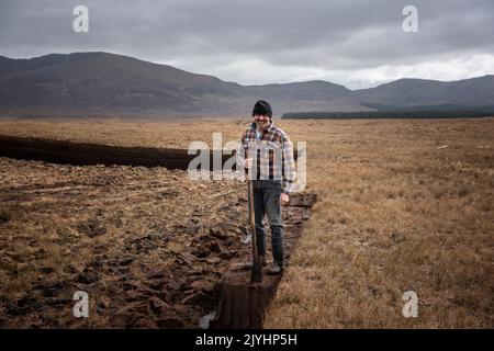 Ein Rasenmäher mitten im ausgedehnten Torfmoor am Rande des Ballycroy-Nationalparks. Er schneidet seinen Rasen von Hand, mit einem Sléan. Stockfoto