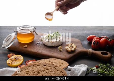 Der Camembert-Käse ist rund, gegrillt, mit goldenem Honig auf einem hölzernen Schneidebrett gegossen. Weicher selektiver Fokus, schwarzer Hintergrund.Platz zum Kopieren. Gesunde Ernährung. Stockfoto