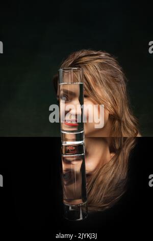 Teilen. Moderne Kunstfotografie. Das Gesicht des schönen Mädchens durch ein Glas Wasser. Objektverzerrung, optische Täuschung. Minimalistische zeitgenössische Kunst Stockfoto