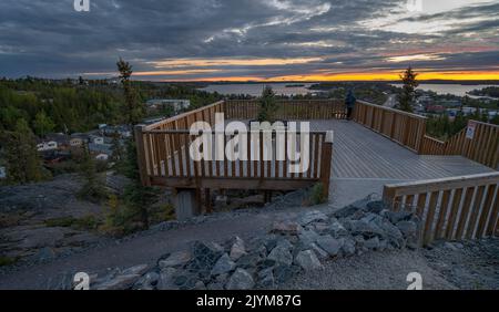 Eine nicht erkennbare Person steht an einem Aussichtspunkt und beobachtet den Sonnenaufgang über der Altstadt in Yellowknife Stockfoto