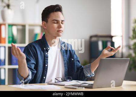 Porträt Eines Jungen Männlichen Angestellten, Der Am Arbeitsplatz Meditiert Stockfoto