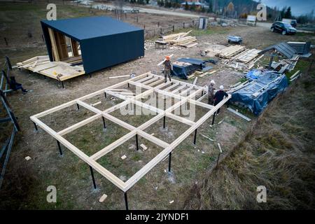 Männer Arbeiter bauen Holzrahmenhaus auf Pfahlfundament. Zimmerleute installieren Holzbalken. Schreinerei-Konzept. Stockfoto