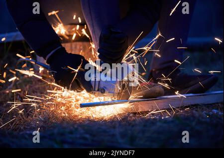 Nahaufnahme der Arbeiter, die Metall schneiden, mit Kreissäge am Abend. Konstruktionskonzept. Stockfoto