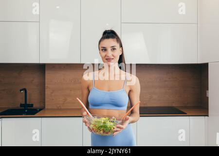 Junge schöne Ernährungsberaterin zeigt frischen Gemüsesalat, schaut lächelnd in die Kamera Stockfoto