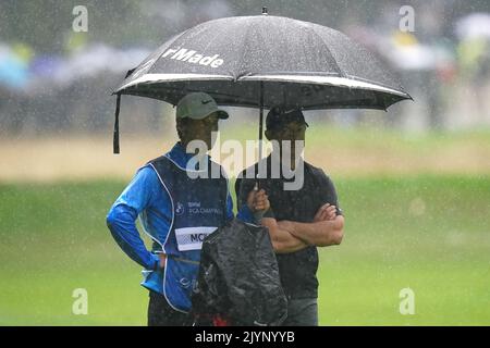 Der nordirische Rory McIlroy (rechts) mit dem Caddy Harry Diamond, der sich am ersten Tag der BMW PGA Championship im Wentworth Golf Club, Virginia Water, vor dem Regen auf dem Fairway 17. schützt. Bilddatum: Donnerstag, 8. September 2022. Stockfoto