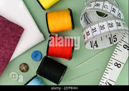 Nähzubehör und Stoff auf grünem Hintergrund. Inklusive Nadel, Faden, Knöpfe und Maßband. Stockfoto