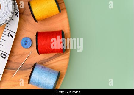 Nähzubehör und Stoff auf grünem Hintergrund. Inklusive Nadel, Faden, Knöpfe und Maßband. Stockfoto