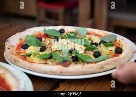 Frische Pizza mit Artischocken, schwarzen Oliven und Basilikumblättern Stockfoto