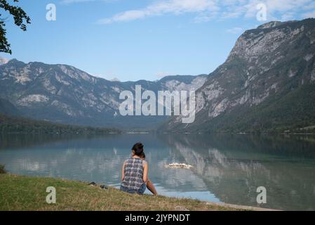 Eine Frau sitzt am Fuße des wunderschönen Bohinj-Sees, dem größten permanenten See Sloweniens Stockfoto