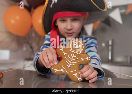 Ein als Pirat gekleideter Junge isst an Halloween Skelett-Lebkuchen und spielt mit Keksen Stockfoto