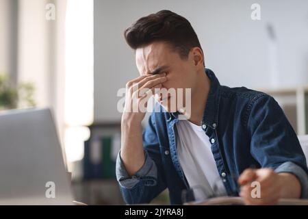 Müde Millennial Guy Leiden Augenbelastung Während Der Verwendung Laptop Im Büro Stockfoto