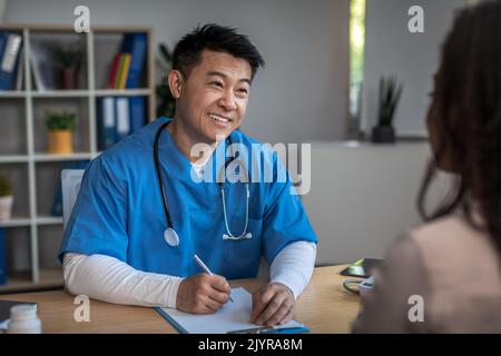 Fröhlich freundlich reifen koreanischen Mann Arzt Beratung junge afroamerikanische Dame Patient in der Klinik Stockfoto