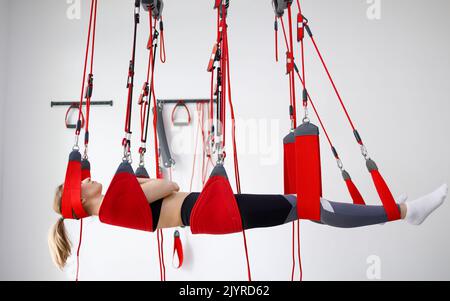 Junge weibliche Patientin hängt am modernen Suspensions-System im Rehabilitationszentrum. Therapeutische Übungen und neuromuskuläre Aktivierung auf der roten Schnur sli Stockfoto