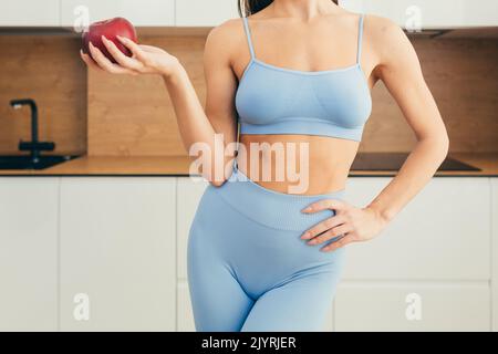 Nahaufnahme eines Körperteils, einer jungen Fitnessfrau, die zu Hause einen roten Apfel in der Hand hält Stockfoto