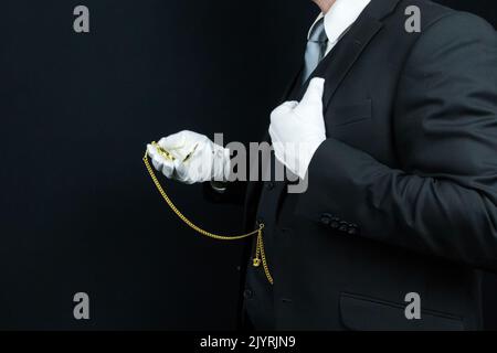 Profil Porträt von Butler in Dunkelanzug und weißen Handschuhen Holding Gold Taschenuhr. Konzept der Dienstleistungsbranche. Stockfoto