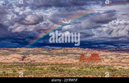 Ein Regenbogen über einem Sandsteinmonolith mit stürmischem Himmel über dem Arches National Park, Moab, Utah. Stockfoto