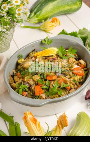 Im Ofen gebackenes Gemüse mit Gewürzen und Kräutern in einer Auflaufform auf weißem Holzhintergrund. Stockfoto