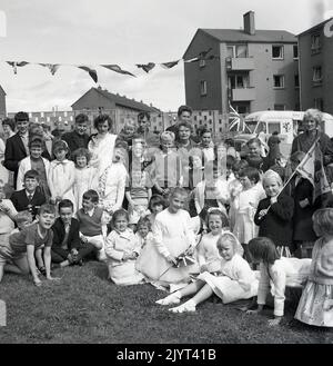 1965, historische, Kinder und Erwachsene versammelten sich für ein Gruppenbild, einige mit Fahnen, darunter ein Gewerkschaftsjacker, nach der Teilnahme an der North Queensferry Gala Day, Fife, Schottland, Großbritannien. Im Hintergrund ist ein Mr-Eiswagen der damaligen Zeit zu sehen. Stockfoto