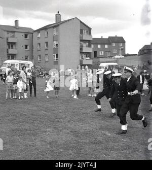 1965, historische, uniformierte Marineoffiziere, die an einem dreibeinigen Rennen auf einem Feld in einem Wohngebiet in North Queensferry, Edinburgh, Schottland, Großbritannien, im Rahmen des North Queensferry Gala Day, einem Gemeinschaftstag für die Bewohner des Anwesens, teilnehmen, Stockfoto