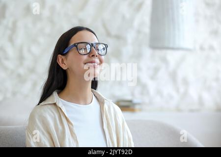Zeit für Yoga. Nahaufnahme. Porträt einer attraktiven jungen Frau mit Brille, die zu Hause in der Lotusposition mit geschlossenen Augen auf einem Sofa sitzt. Ruht sich aus, entspannt sich Stockfoto