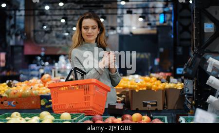 Kaukasische Frau Verbraucher weibliche Shopper Mädchen Käufer mit Warenkorb im Lebensmittelgeschäft im Supermarkt die Wahl orange saftige Zitrusfrüchte köstliche Früchte Stockfoto